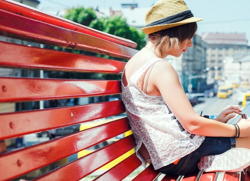 City stylish hipster tourist young woman, sitting on a red bench, using digital tablet.
