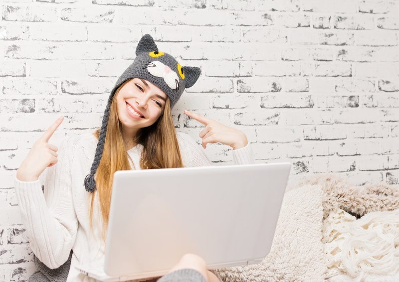 Young woman at home in cute cat beanie hat using laptop chatting
